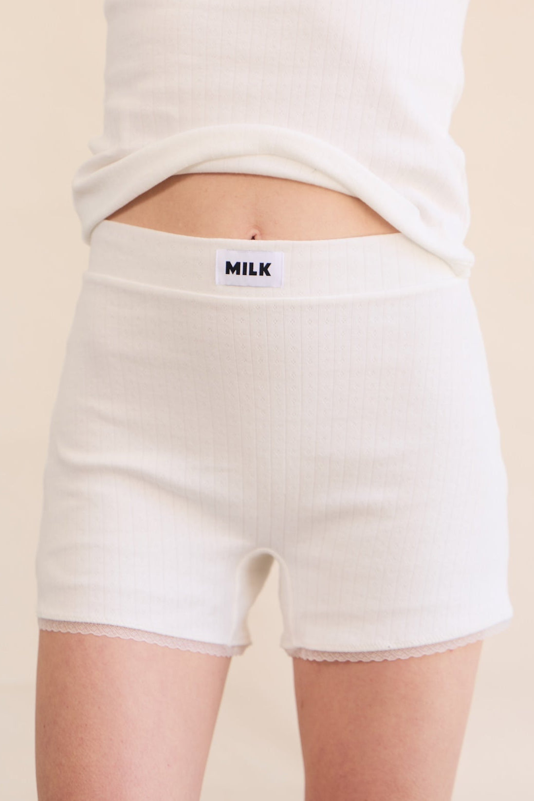 A model wearing a matching Pointelle ribbed lounge shorts with leakproof singlet top with a small black 'MILK' brand label on the waistband.